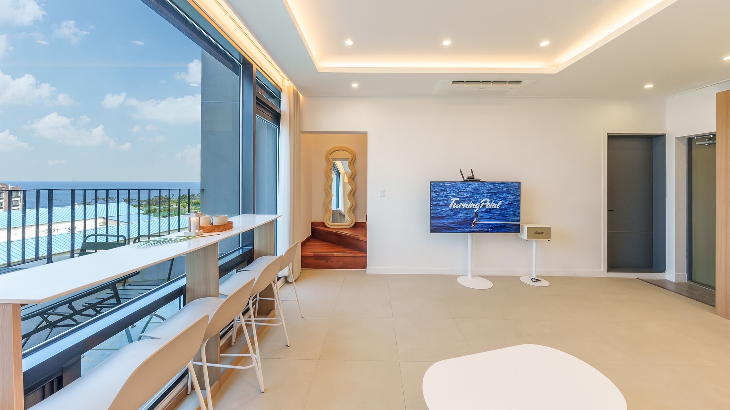 A modern hotel room with a balcony, a large TV screen, and a view of the ocean.