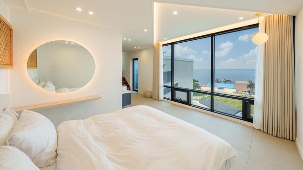 Ein modernes Schlafzimmer mit einem großen Bett, einem runden Spiegel und einem Balkon mit Meerblick.