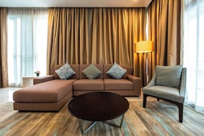 A modern living room with a sectional sofa, a round coffee table, and a single armchair. - Cozy 3BR Somerset, Puteri Harbour, Legoland (Iskandar Puteri)