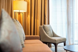 A hotel room with a sofa, armchair, lamp, and a view of the outdoors. - Cozy 3BR Somerset, Puteri Harbour, Legoland (Iskandar Puteri)
