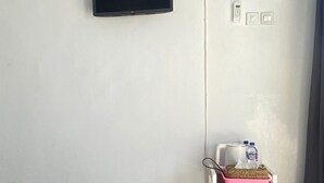 Une pièce avec un téléviseur à écran plat fixé au mur, une étagère blanche sur laquelle repose un plateau rose, et un radiateur blanc.