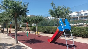 A playground with a red slide, a blue swing set, and a yellow swing set.