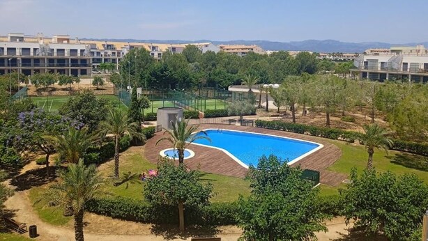 A residential area with a swimming pool surrounded by greenery and a sports field.