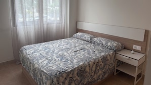 A bedroom with a bed, a nightstand, a lamp, and a window with sheer curtains.