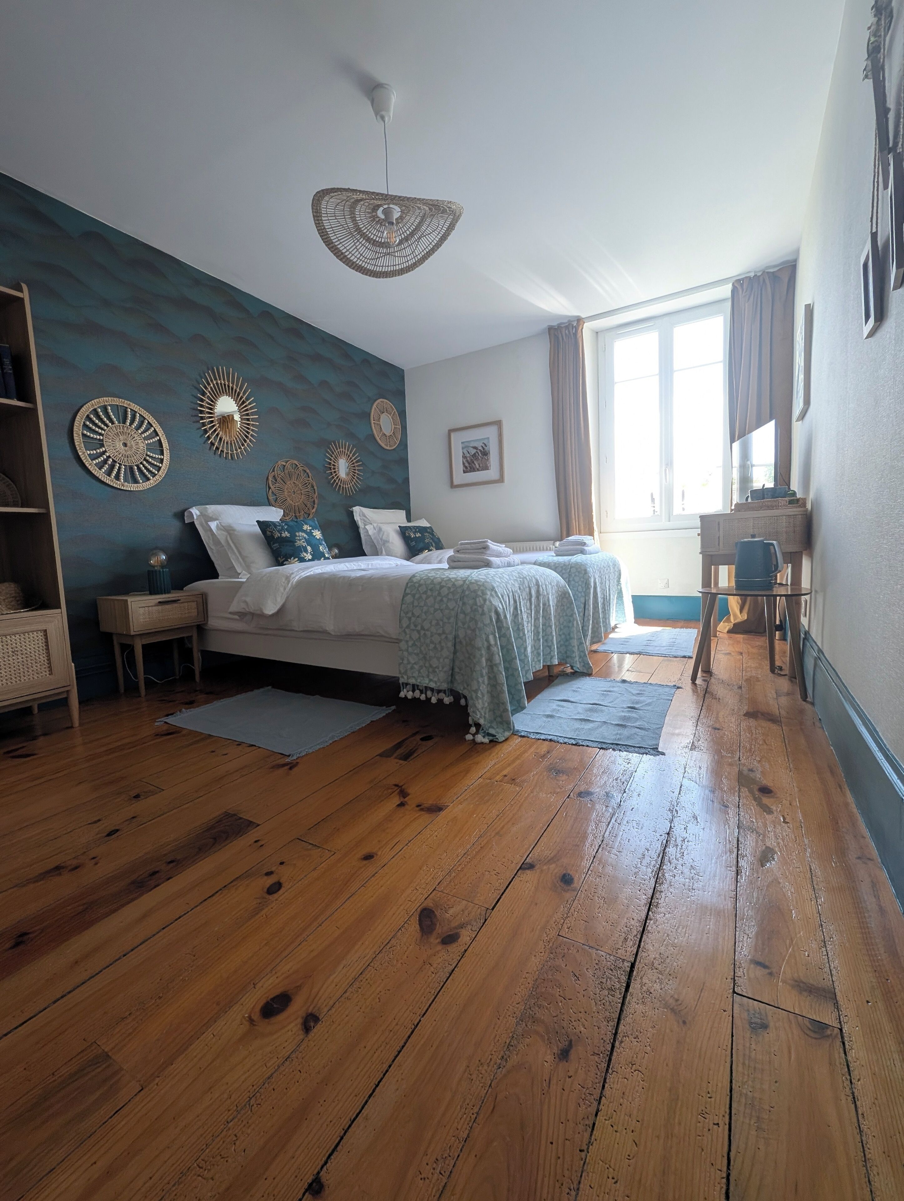 A bedroom with a bed, bedside tables, a dresser, a window with curtains, and a ceiling fan.