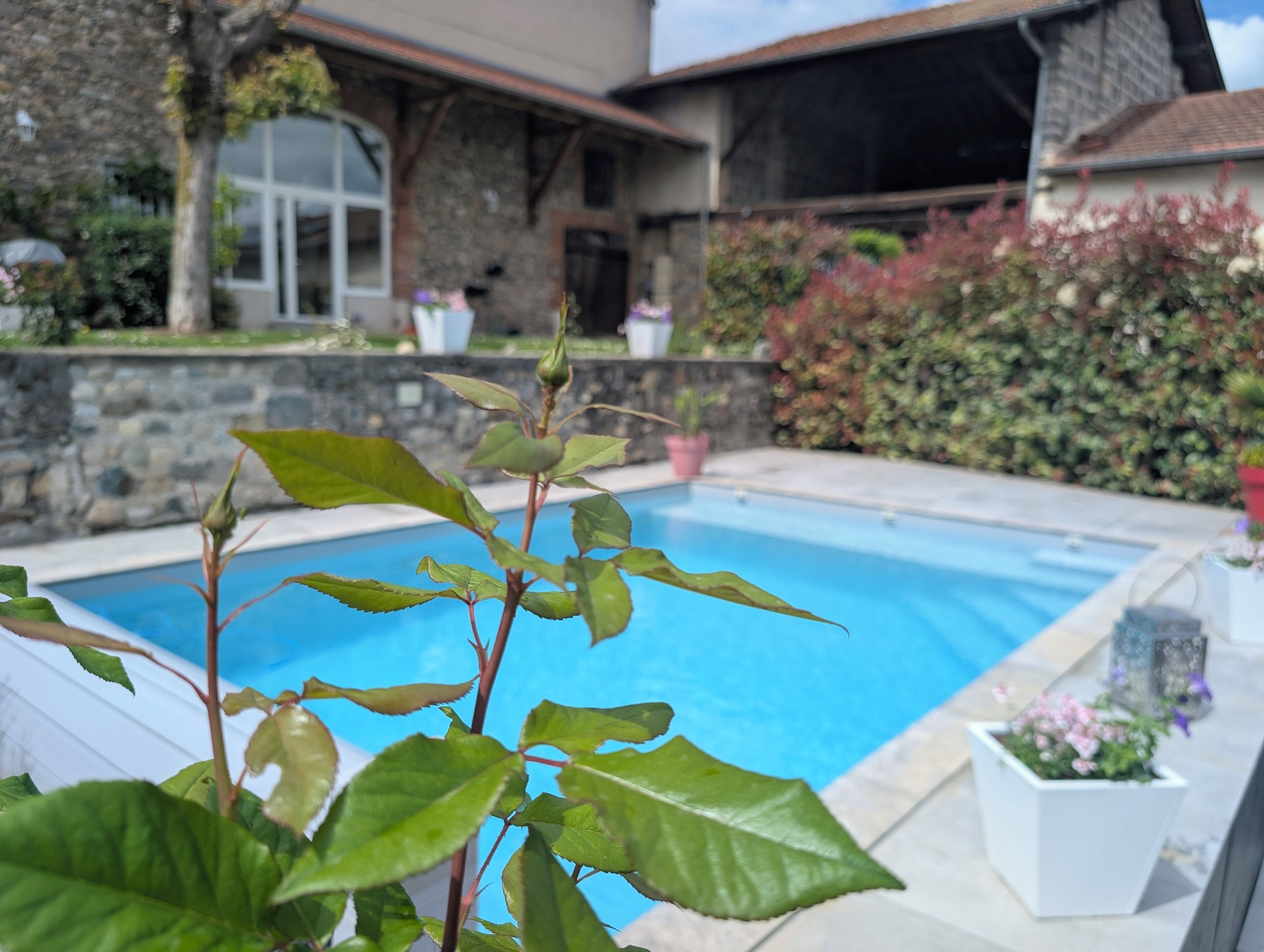 A swimming pool with a stone wall and a house in the background.