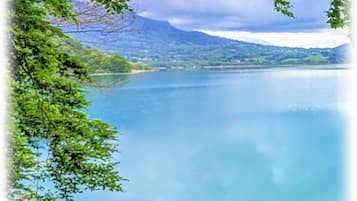 A serene lake with clear blue water, surrounded by lush greenery and mountains in the background.