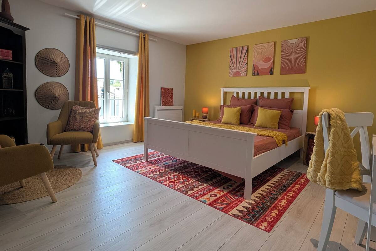 A bedroom with a bed, a chair, a bookshelf, and a window.