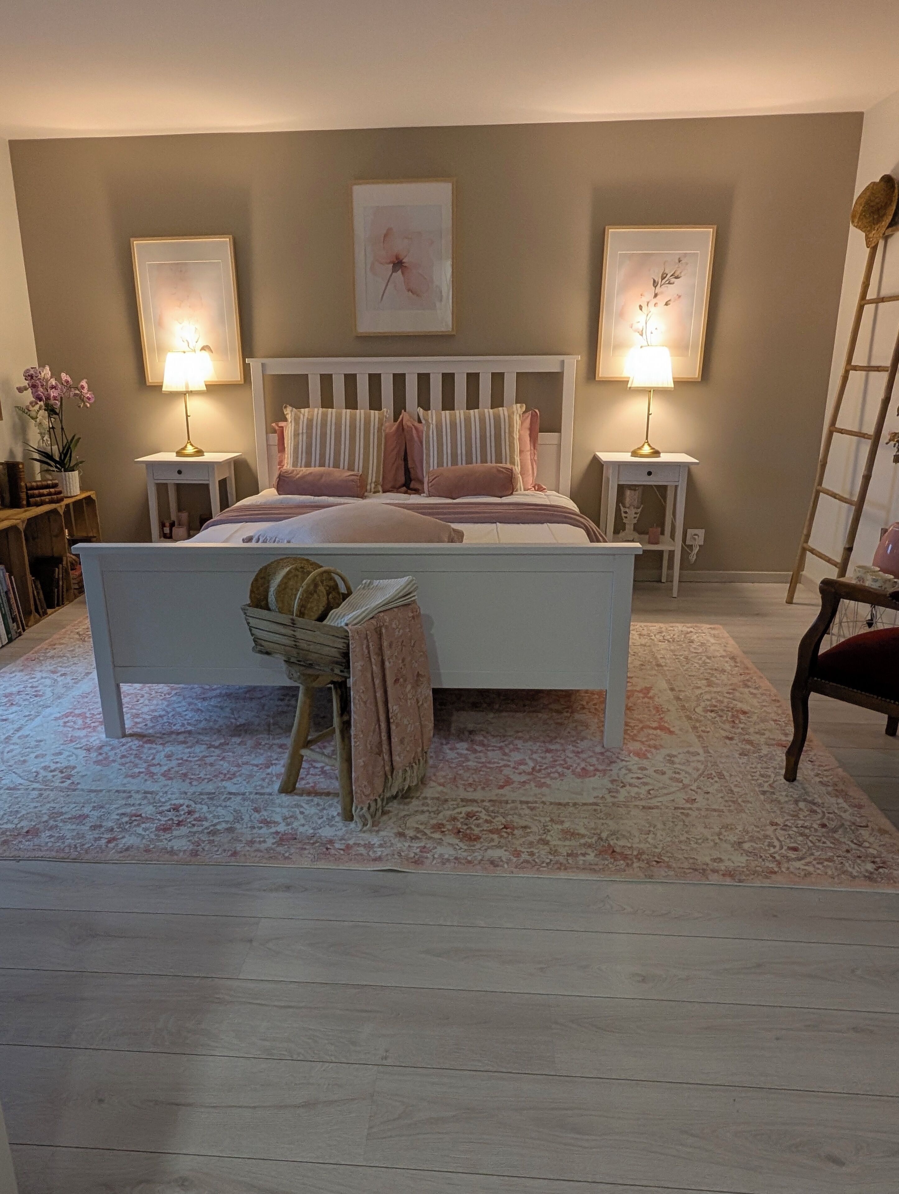 A bedroom with a large bed, two bedside tables with lamps, a wooden bench, and a ladder.