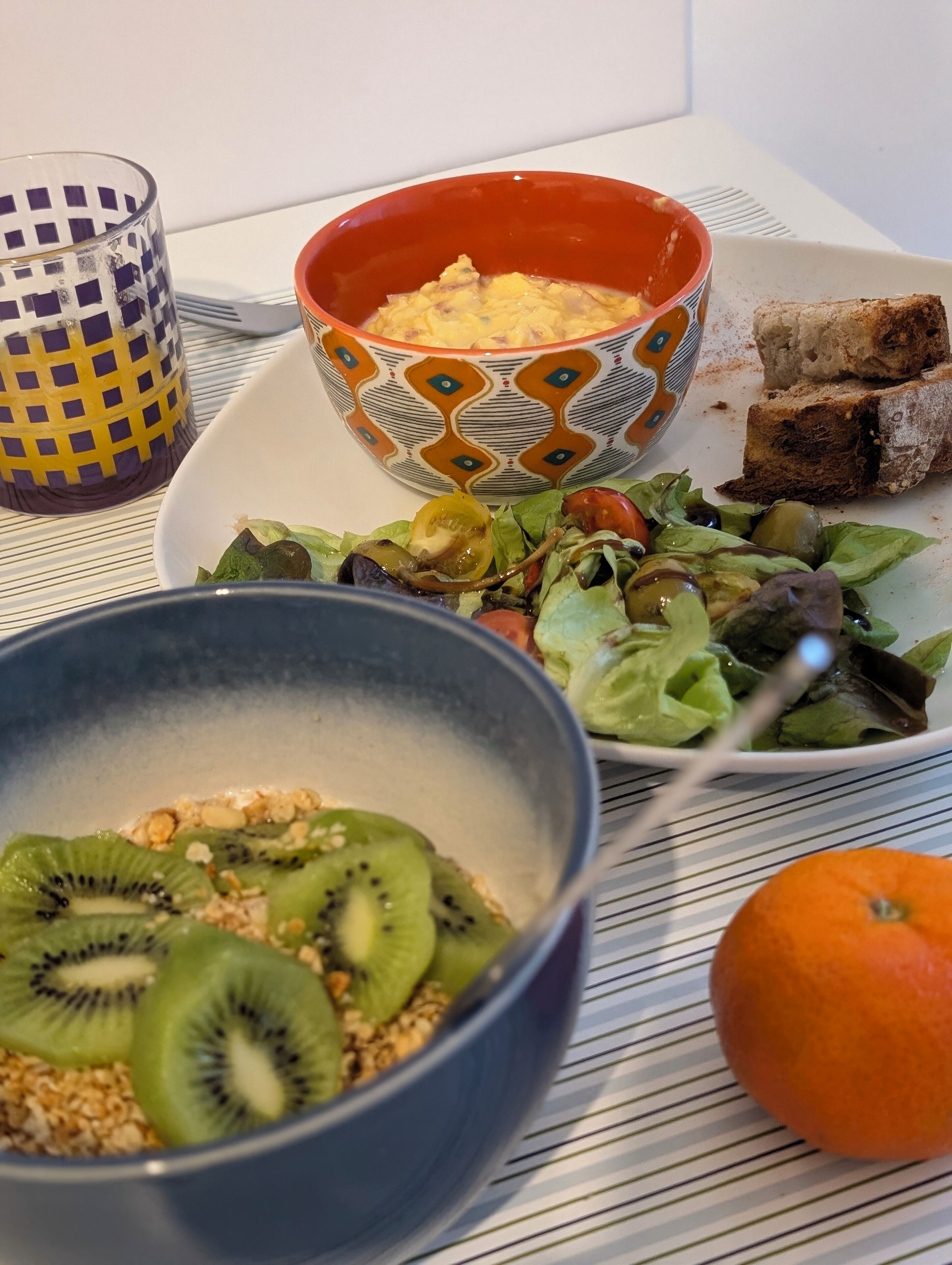 A meal with a bowl of scrambled eggs, a plate of salad, and slices of bread on a table.