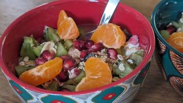 A bowl of fruit salad with a spoon, containing oranges, pomegranate seeds, and other fruits, in a colorful bowl with a geometric pattern.