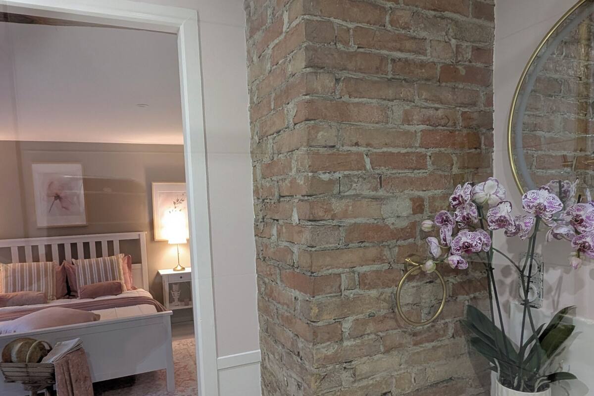 A bedroom with a brick accent wall, a white dresser with a mirror, and a bed with striped bedding.