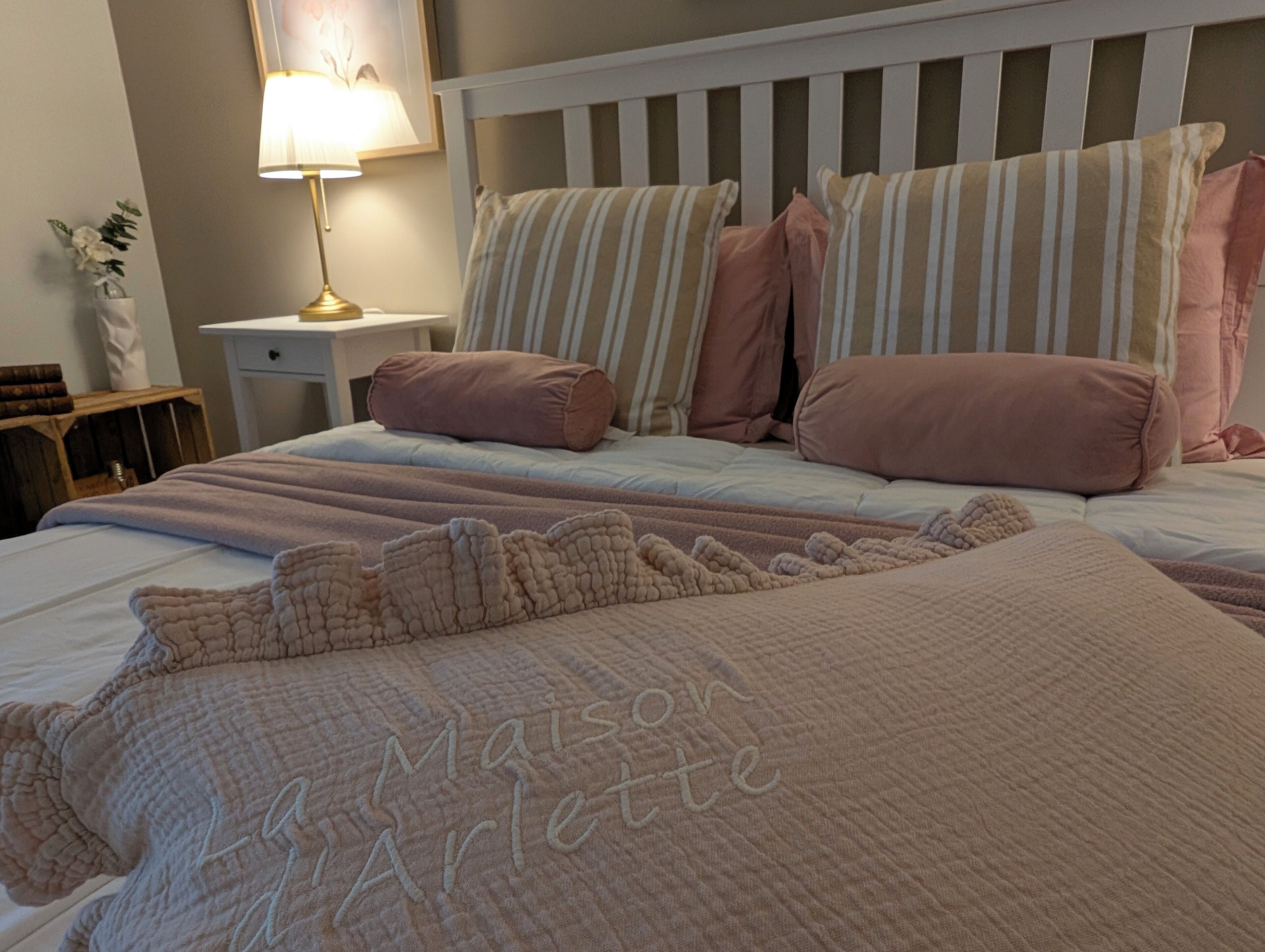 Une chambre à coucher avec une tête de lit blanche, des coussins à rayures et une courtepointe ornée de motifs brodés.