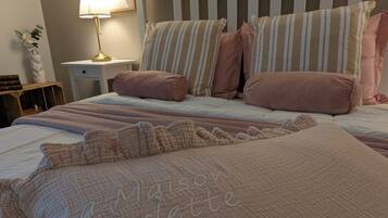 Une chambre à coucher avec une tête de lit blanche, des coussins à rayures et une courtepointe ornée de motifs brodés.
