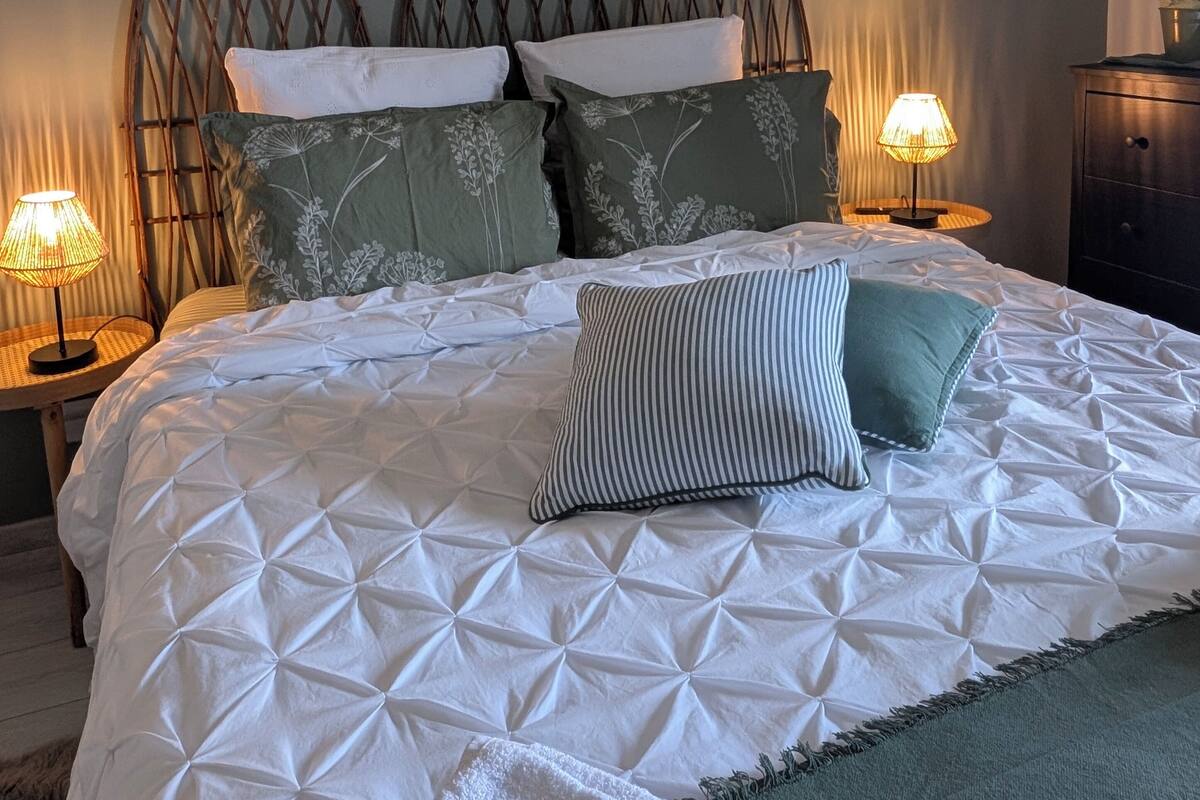 A neatly made bed with a white quilt and decorative pillows, flanked by two wall-mounted lamps.