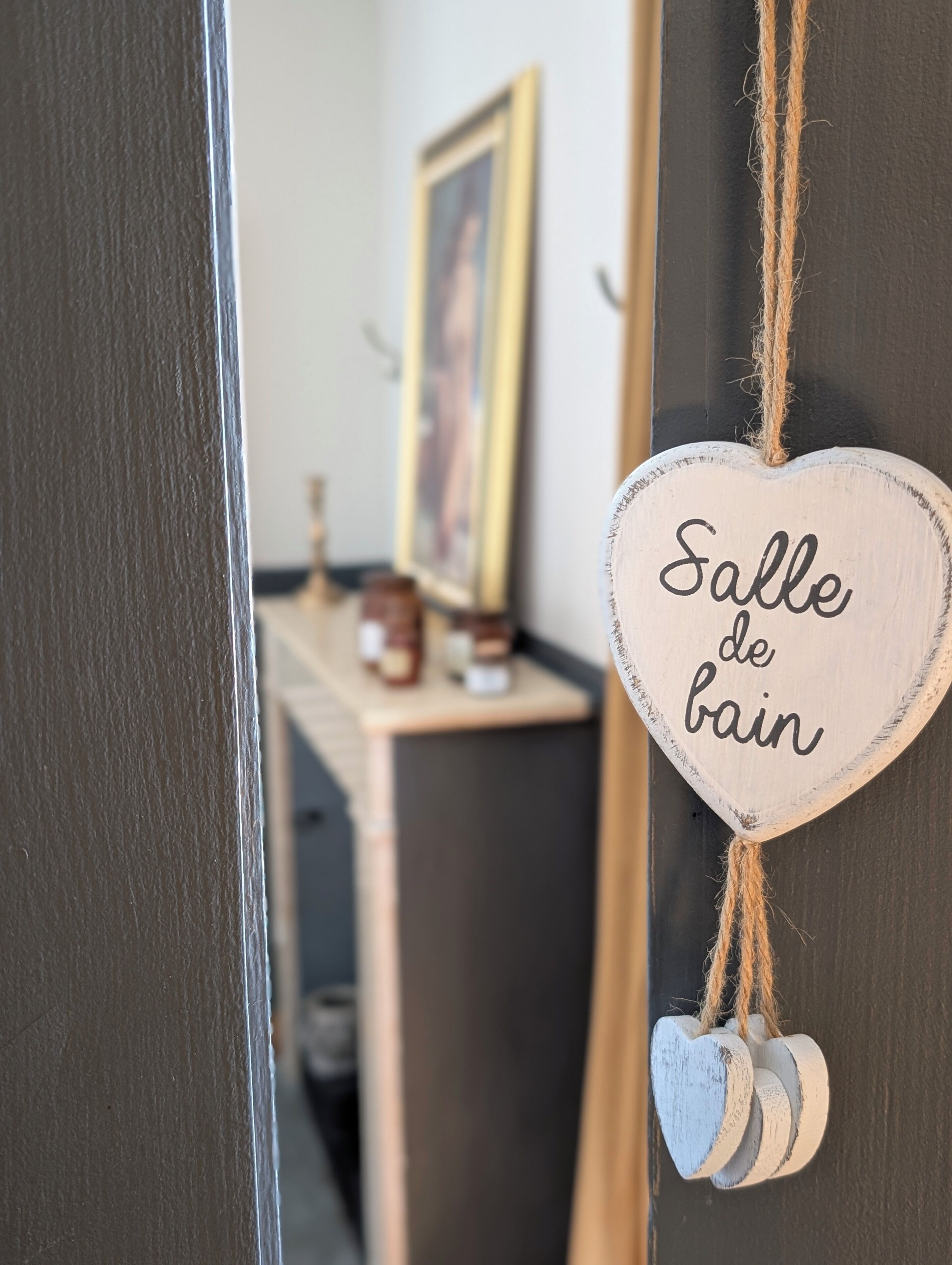 A wooden door with a heart-shaped sign that reads "Salle de bain" (bathroom) and a small heart-shaped decoration hanging below it.