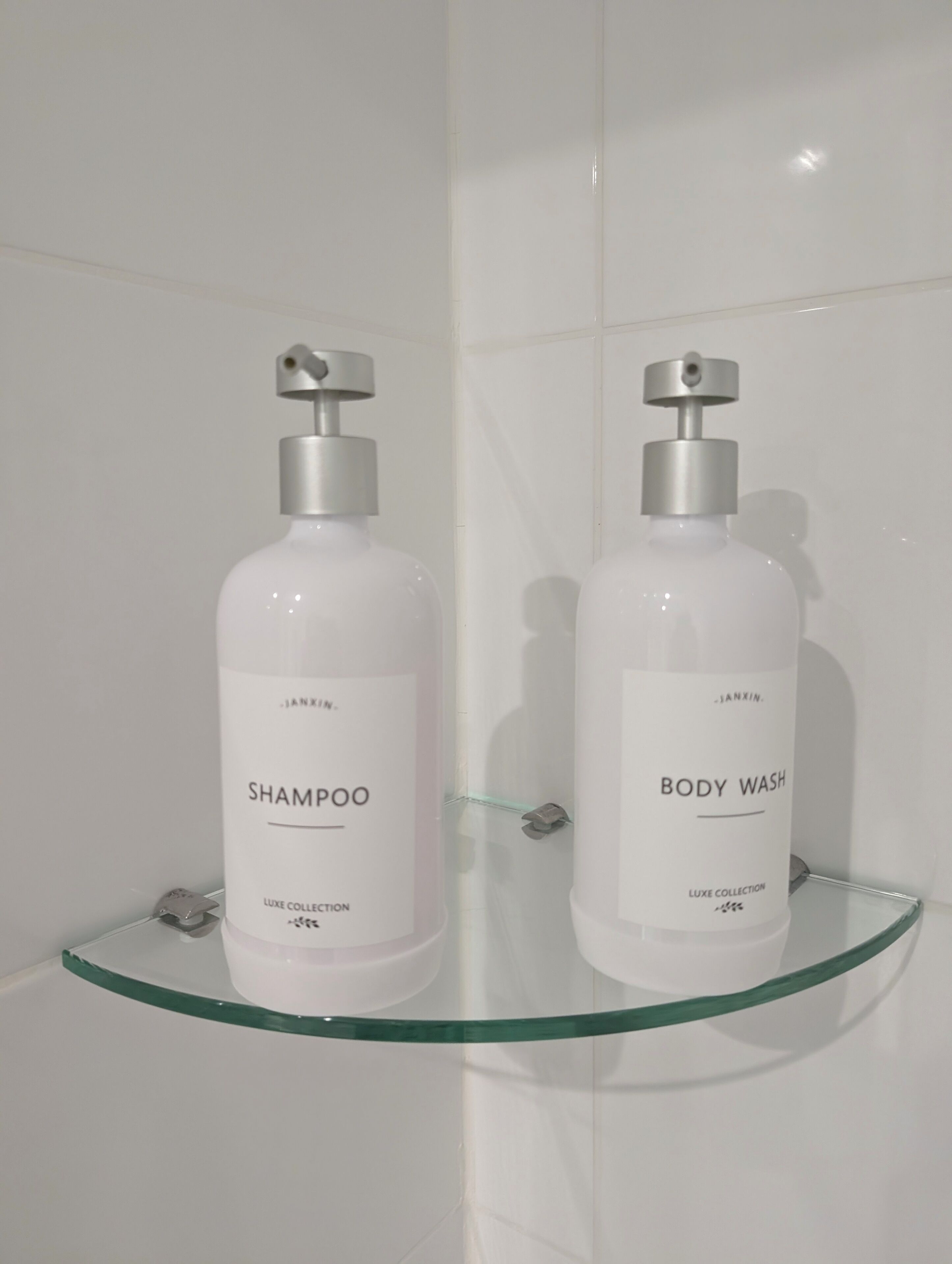 To shampoo- og brusegel-flasker på en glashyld i et badeværelse.