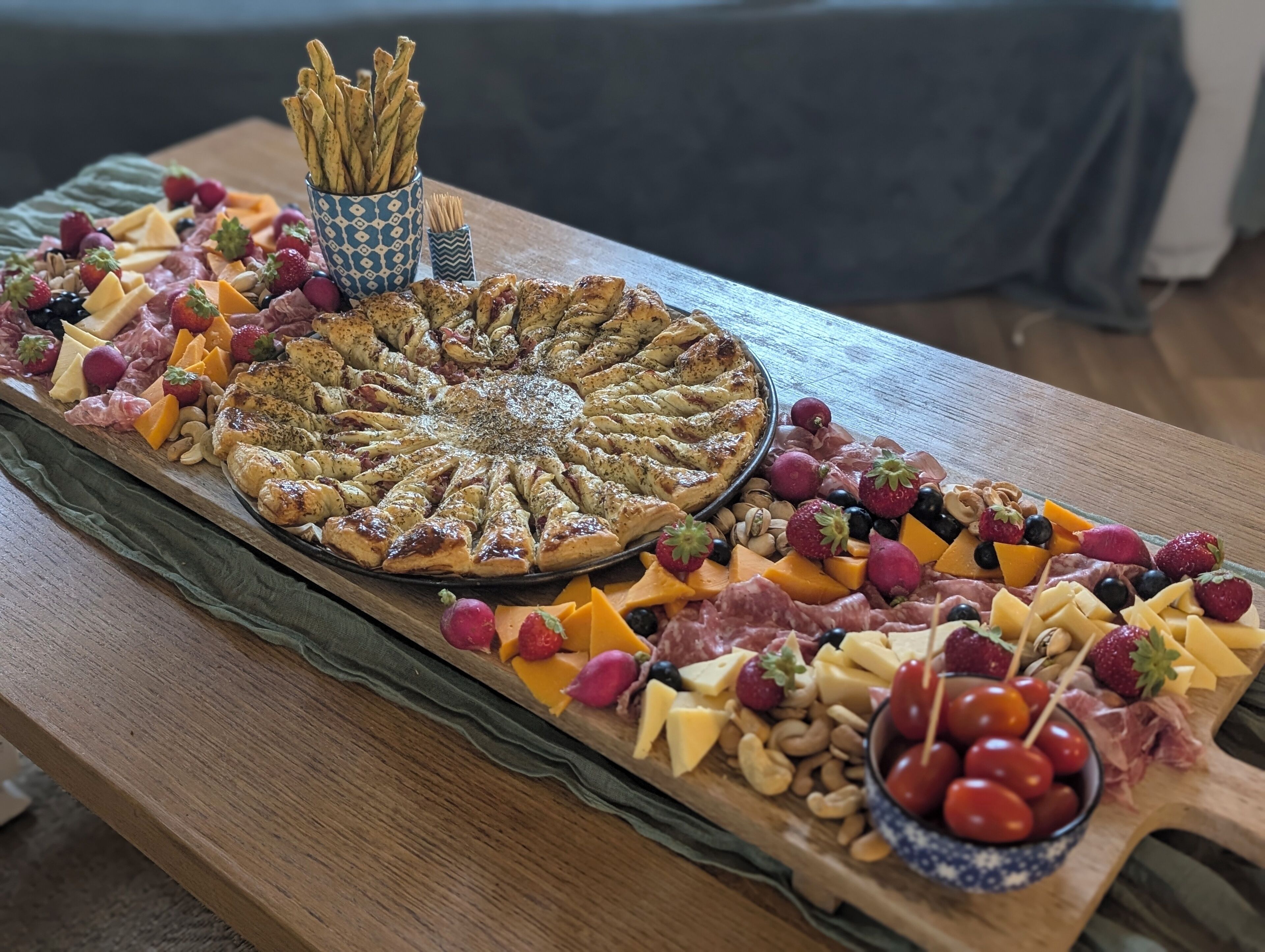 A wooden table with a charcuterie board featuring various cheeses, meats, fruits, and nuts.