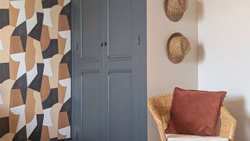 Een kamer met een wand met een geometrisch patroon, een grijze deur, een rieten stoel met kussen en een ronde tafel.