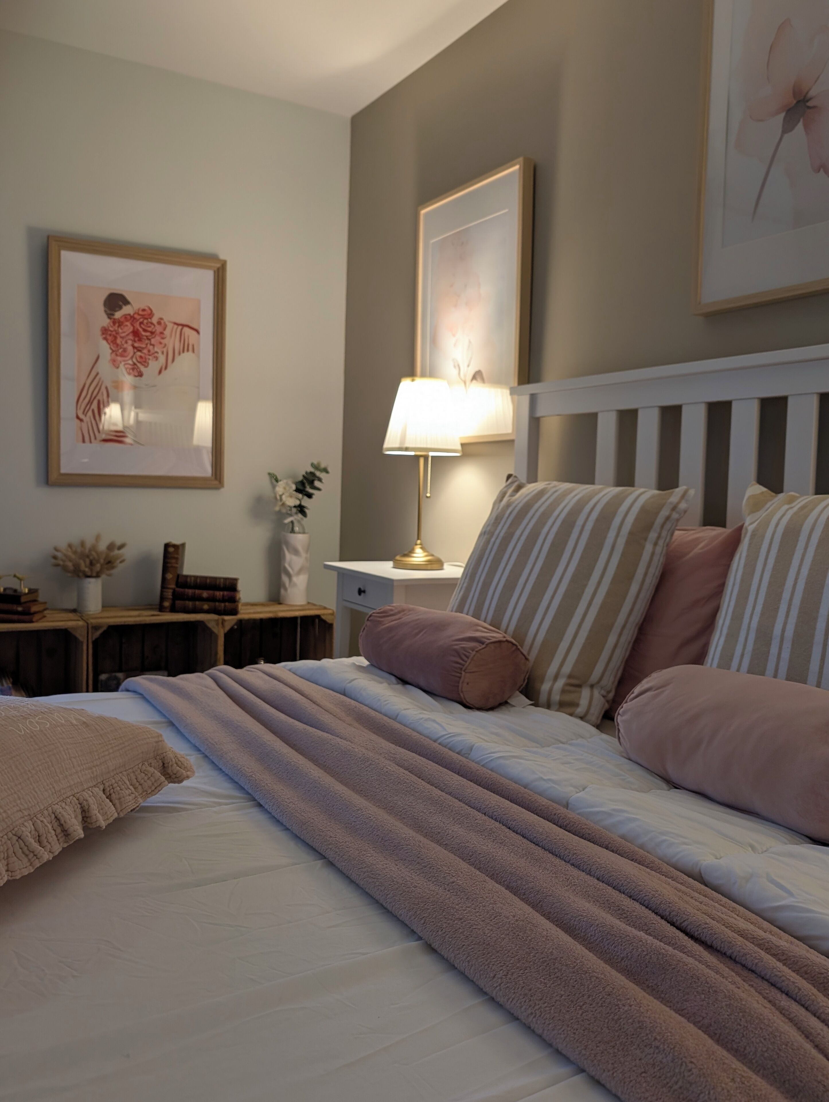 A neatly arranged bedroom with a bed, pillows, a bedside table with a lamp, and framed artwork on the wall.