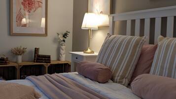 A neatly arranged bedroom with a bed, pillows, a bedside table with a lamp, and framed artwork on the wall.