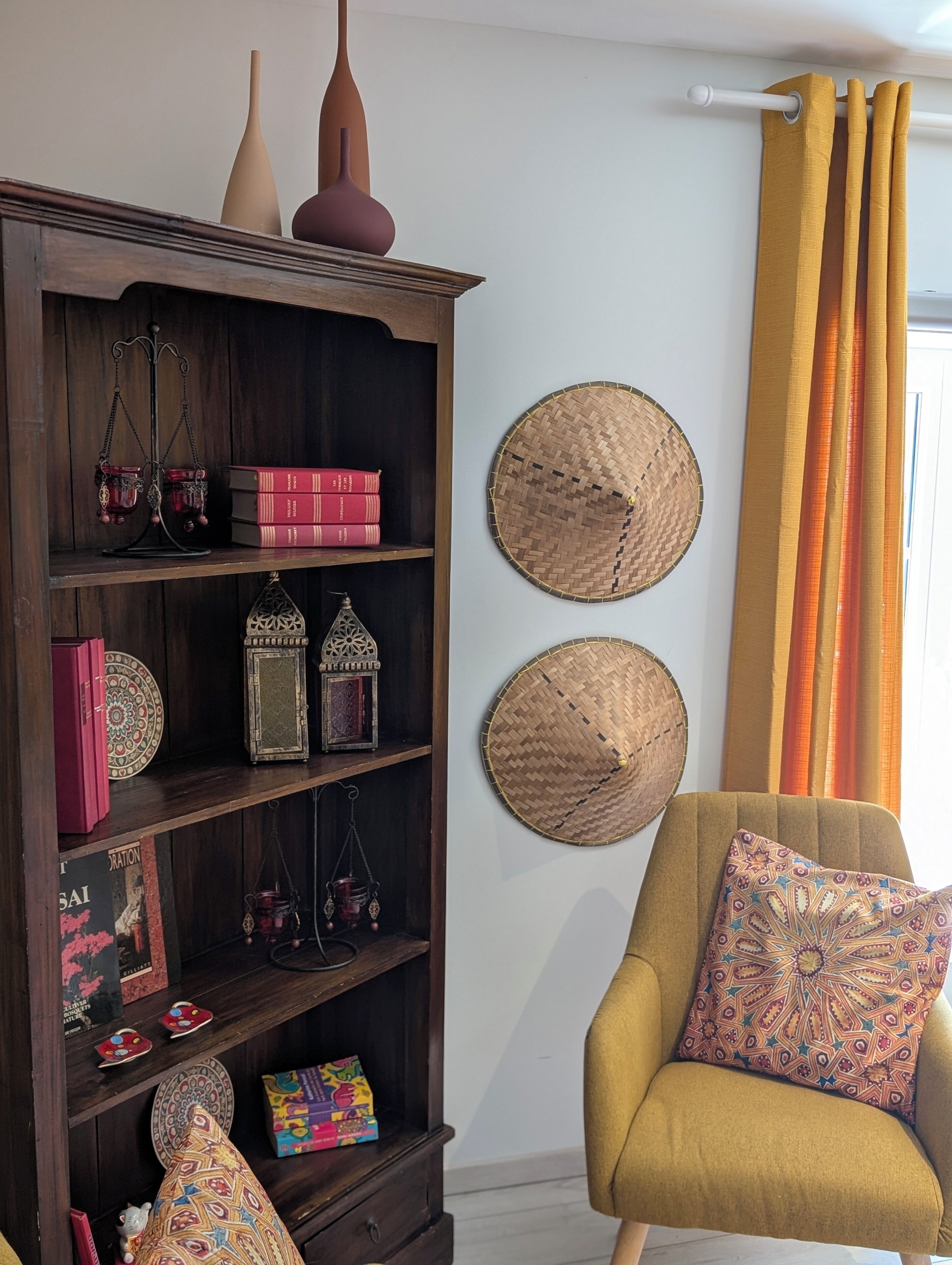 Um quarto com estante de madeira escura, poltrona estampada e itens decorativos trançados na parede.