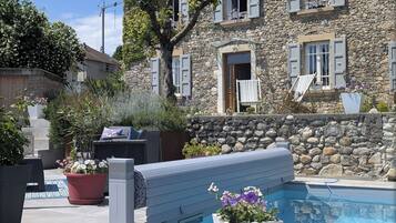 Un edificio de piedra con piscina, mobiliario exterior y jardín.