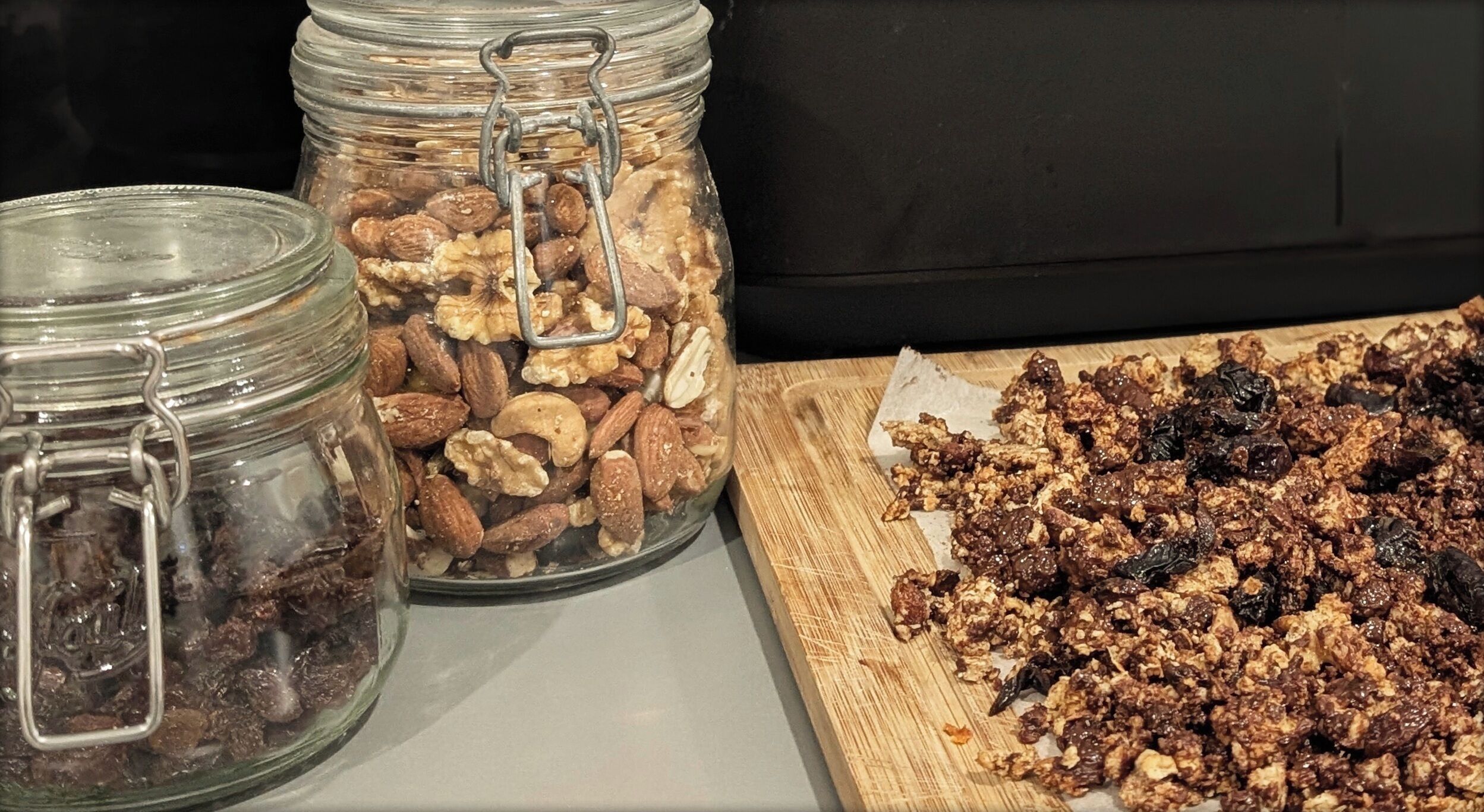 Three glass jars with metal clasps, one containing almonds, another with walnuts, and the third with a mix of nuts and dried fruits.