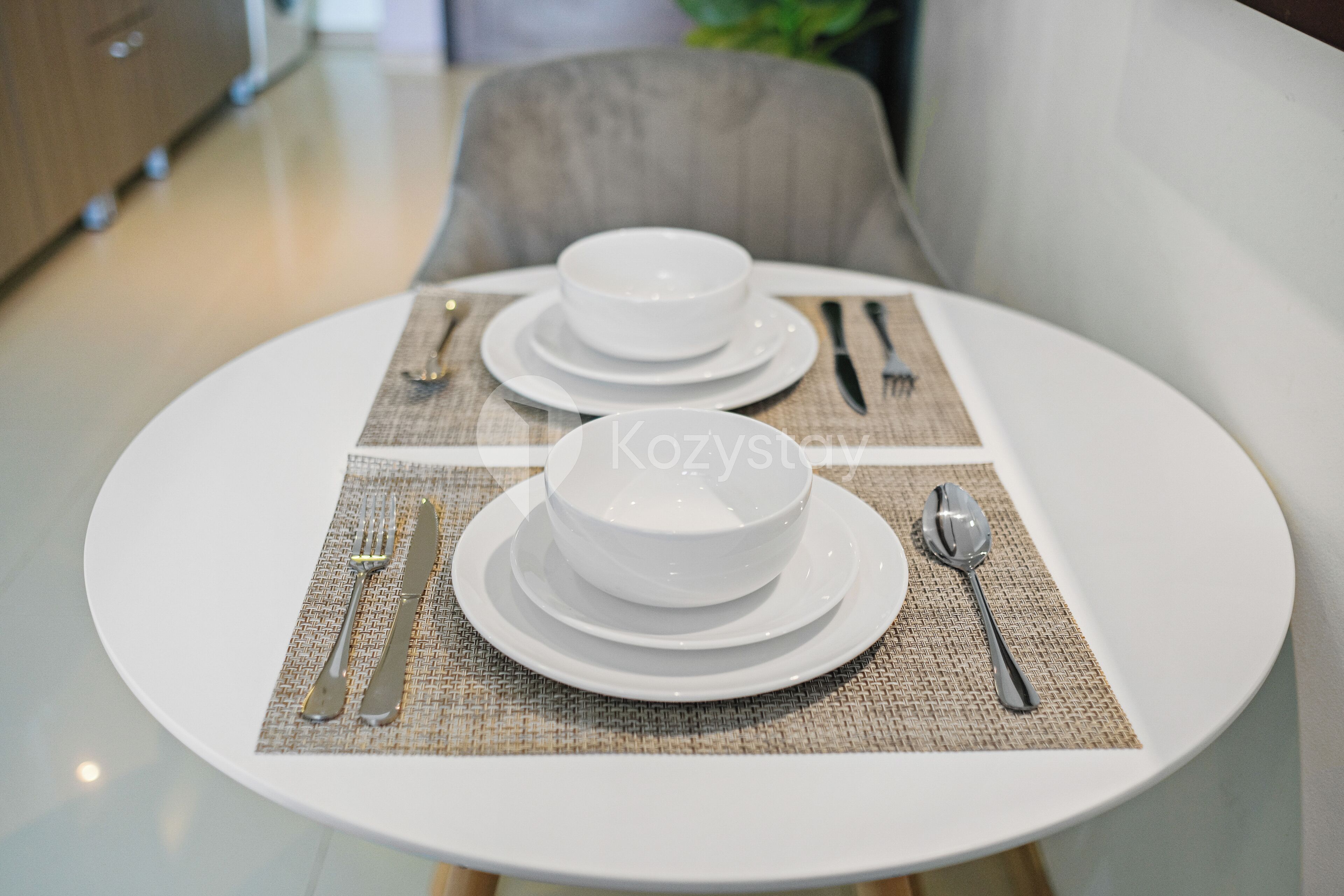 Een eettafel gedekt met witte borden, kommen, bestek en een placemat.