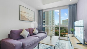A modern living room with a purple sofa, a glass coffee table, and a large window offering a city view.