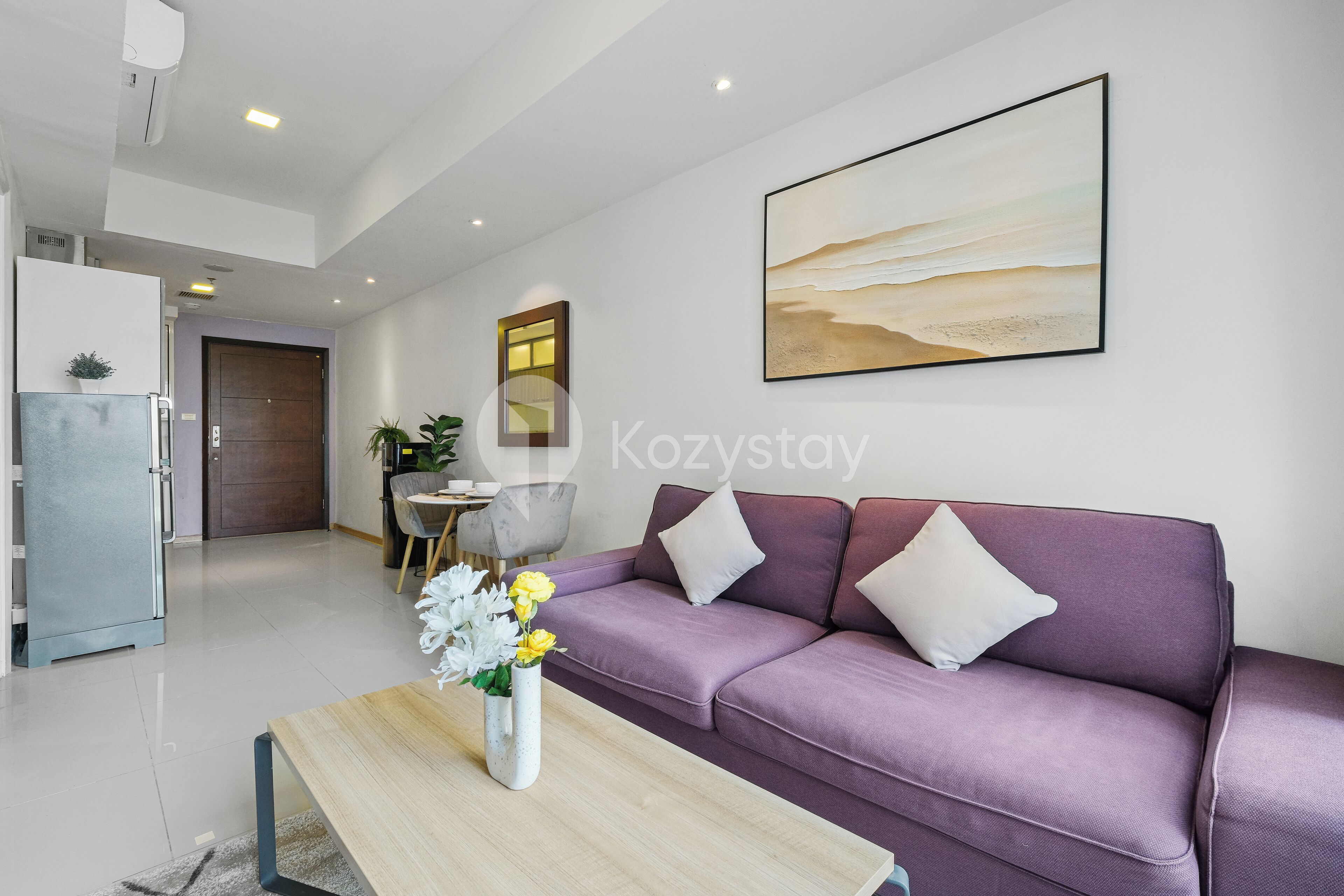 Ein modernes Wohnzimmer mit einem violetten Sofa, einem Couchtisch mit Blumen und einem Gemälde an der Wand.