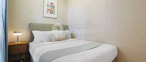 Una cama bien hecha con un cabecero verde, una lámpara de noche y un cuadro en la pared.
