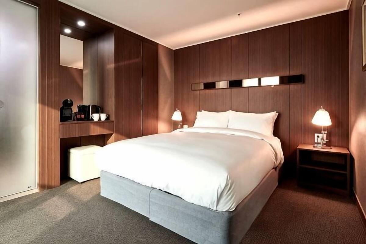 Ein Hotelzimmer mit einem großen Bett, Nachttischlampen, einer integrierten Ablagefläche mit Kaffeemaschine und einem Spiegel.