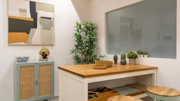 A modern room with a wooden desk, two stools, a rattan cabinet, and a large abstract painting on the wall.