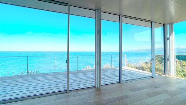 A spacious room with large floor-to-ceiling windows offering a view of the sea. - Cliff House MORAI (Ishikari)