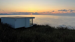 A modern, minimalist building with a glass facade overlooking a calm body of water at sunset. - Cliff House MORAI (Ishikari)