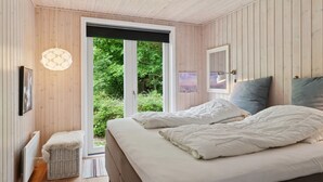 Une chambre à coucher avec un lit, un petit banc, une fenêtre et une lampe fixée au mur.