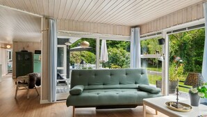 Un salon moderne avec un canapé vert, un parquet en bois et de grandes fenêtres donnant sur un paysage verdoyant.