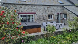 Une maison en pierre avec un toit en pente, une terrasse avec une table et des chaises, et un jardin fleuri.