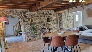 Un coin repas rustique avec un mur en pierre, des poutres en bois au plafond et une table ronde entourée de chaises.