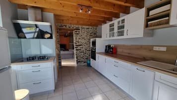 Una cocina con armarios blancos, pared de piedra y techo de madera.