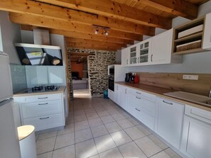 Une cuisine avec des armoires blanches, un mur en pierre et un plafond en bois.