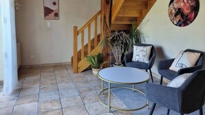 Une pièce chaleureuse avec un escalier en bois, deux fauteuils avec des coussins, une petite table et une plante en pot.