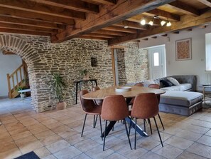 Un espace repas agrémenté d’un mur en pierre, de poutres en bois et d’une table ronde entourée de chaises.