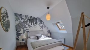 Une chambre avec un grand lit, une table de chevet avec des lampes, un radiateur, un plancher en bois et un mur orné d’un motif de feuilles.