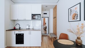 A modern kitchen with white cabinets, a microwave, and a dishwasher. There is a dining area with a bench and a table with woven placemats. - Charming Studio by Park - Historic Center (Chișinău)