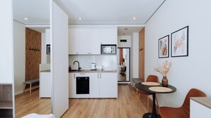 A modern kitchen with white cabinets, a microwave, and a dishwasher. There is a dining area with a table and chairs, and a bench in the corner. - Charming Studio by Park - Historic Center (Chișinău)