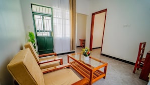Une pièce comprenant un canapé, une table basse avec un plateau en verre, une plante en pot et une vue sur l’extérieur par une fenêtre ornée de rideaux.