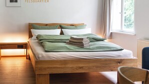 A wooden bed with a headboard, green bedding, and a stack of folded blankets.