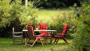 An outdoor seating area with a table and four chairs, surrounded by lush greenery.